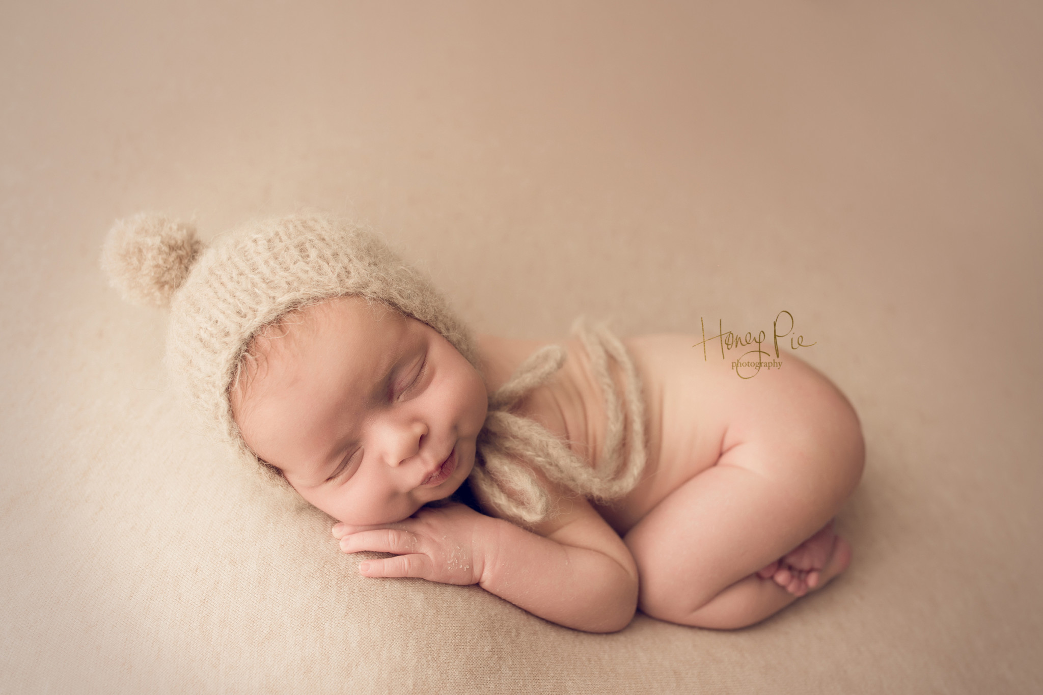 Newborn boy pouting during his photoshoot whilst fast asleep wearing a beige hat