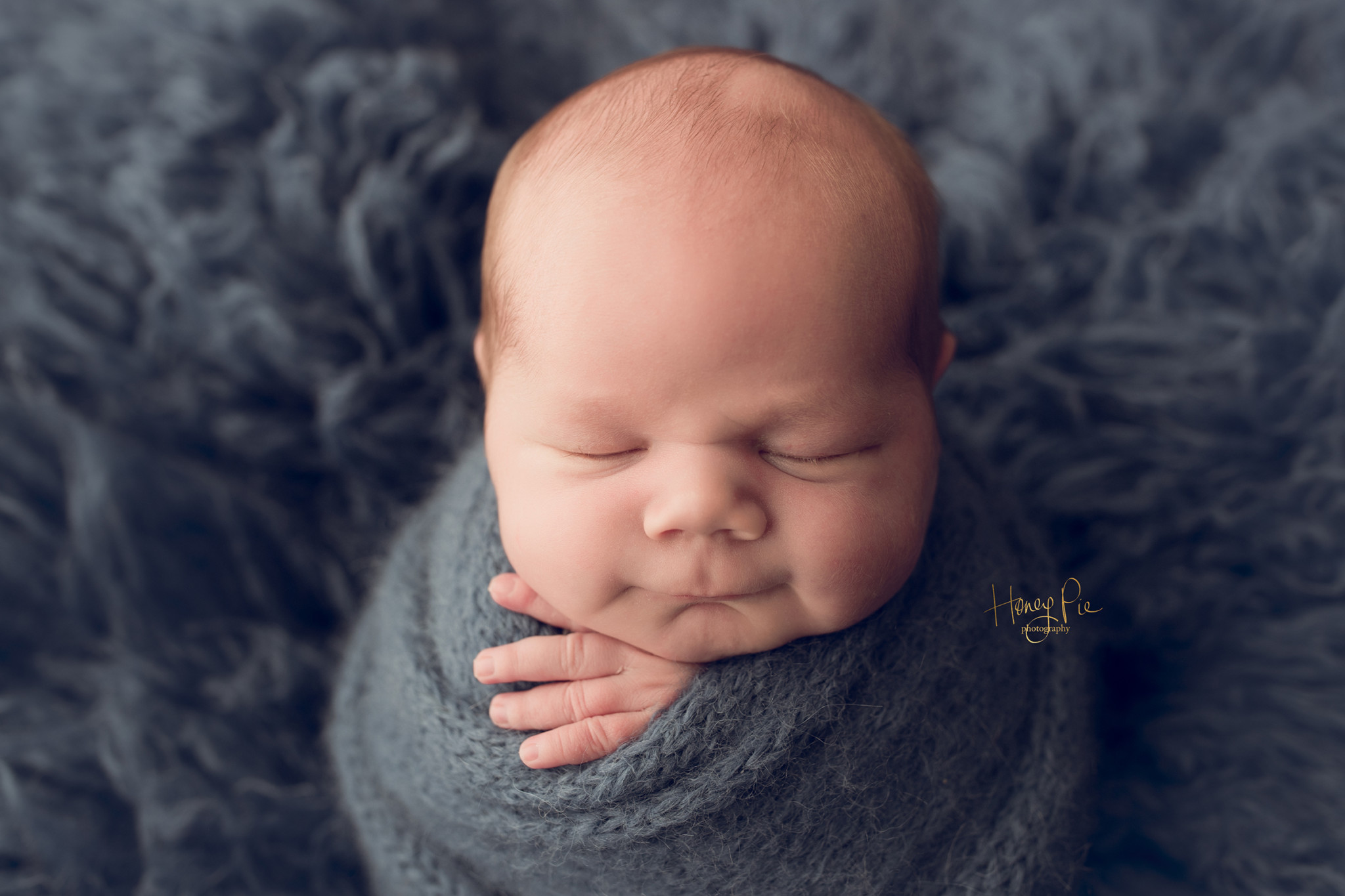 Baby boy smiling whilst swaddled & asleep during baby photoshoot