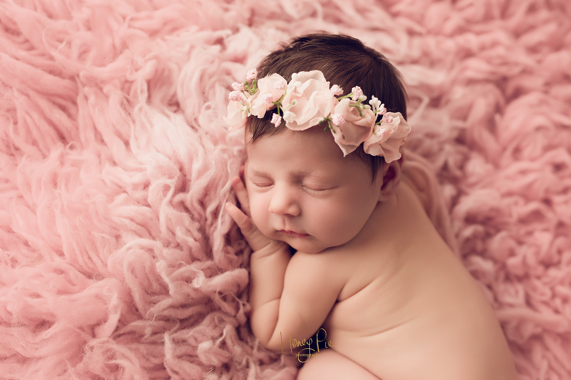 Sleeping newborn baby girl on a pink fluffy blanket wearing a pink flower crown during her newborn photoshoot