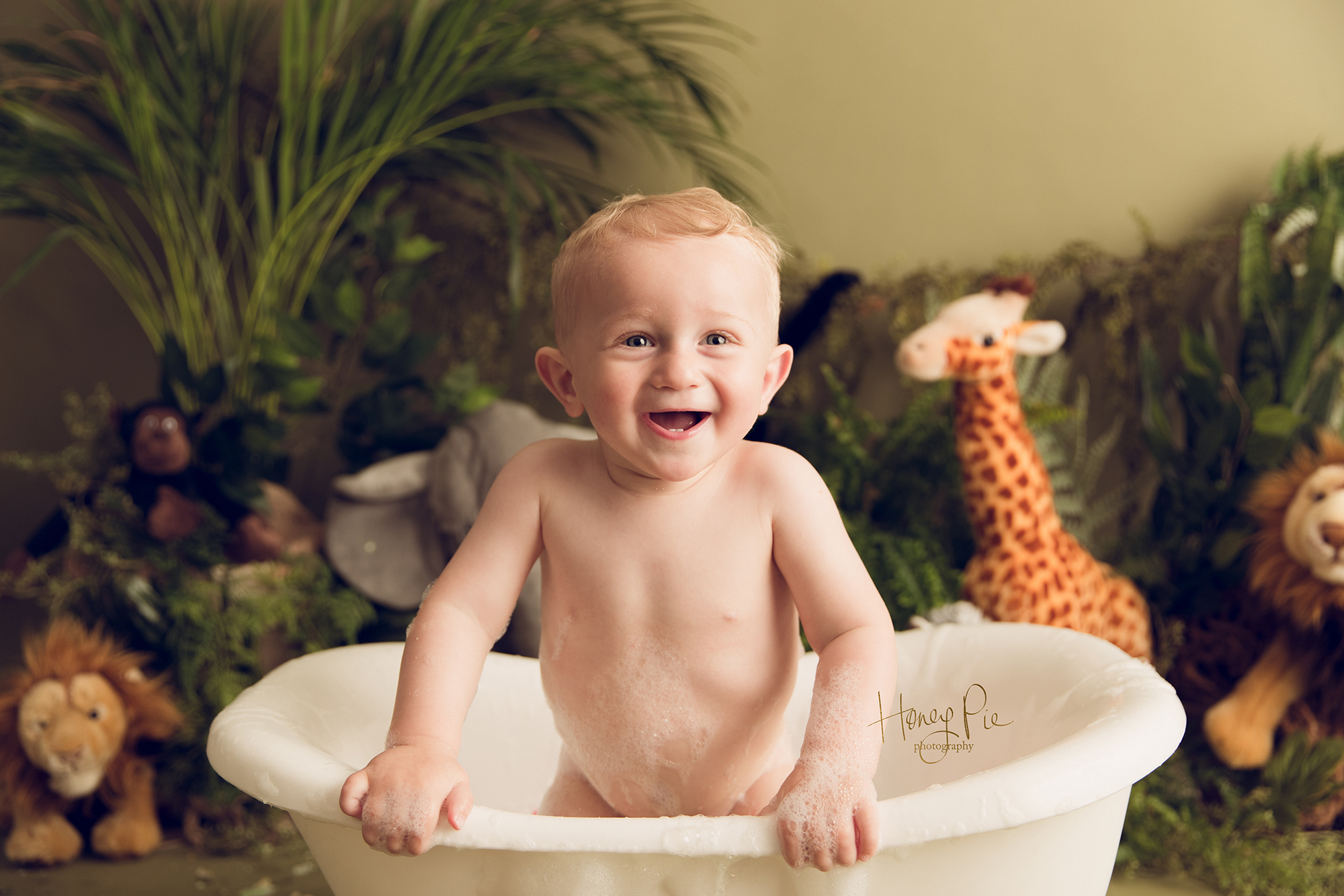 Birthday baby boy with green plants & jungle toys smiling in his bubble bath tub