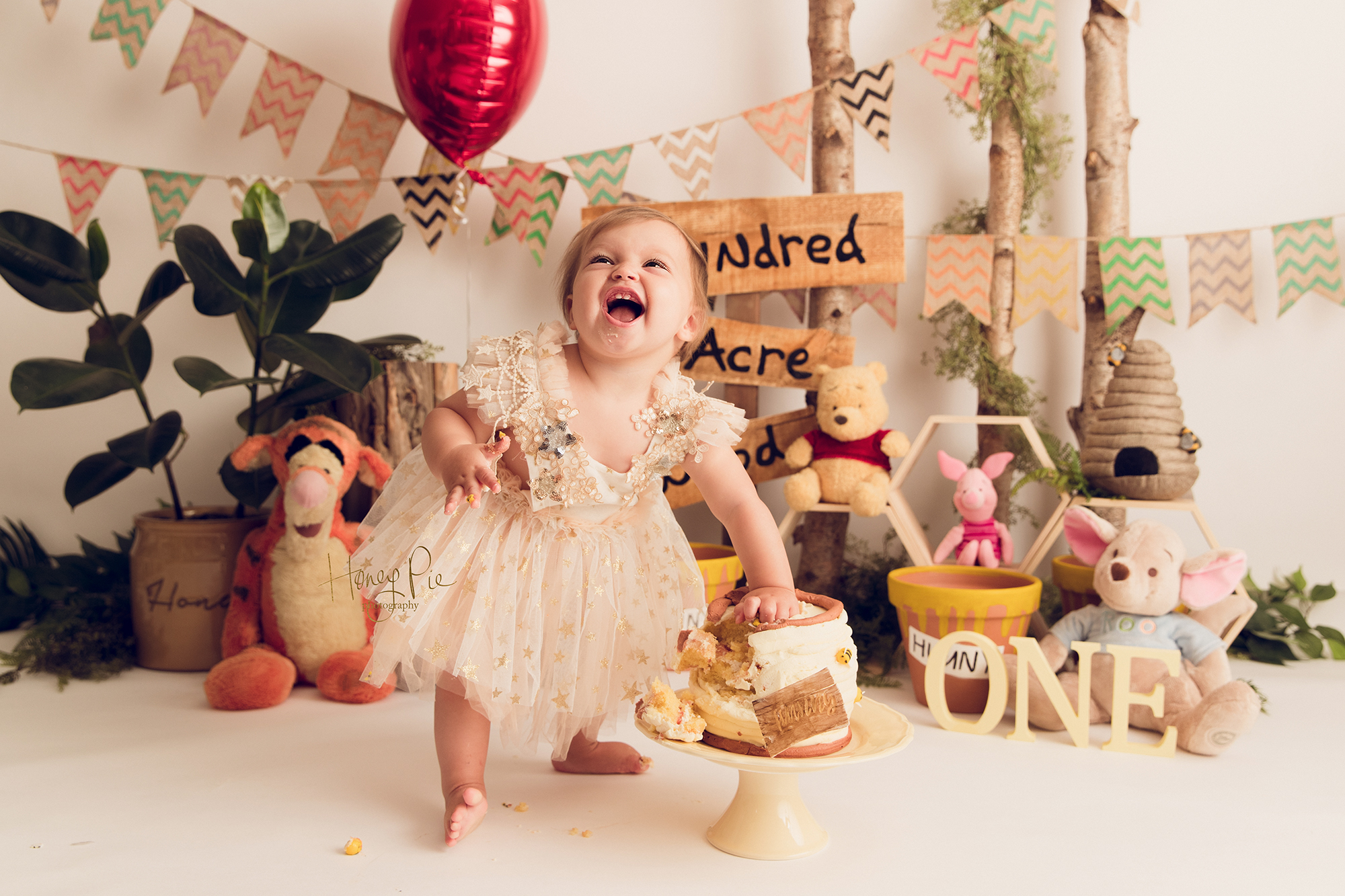 Baby in party dress smashing her Winnie The Pooh themed birthday cake