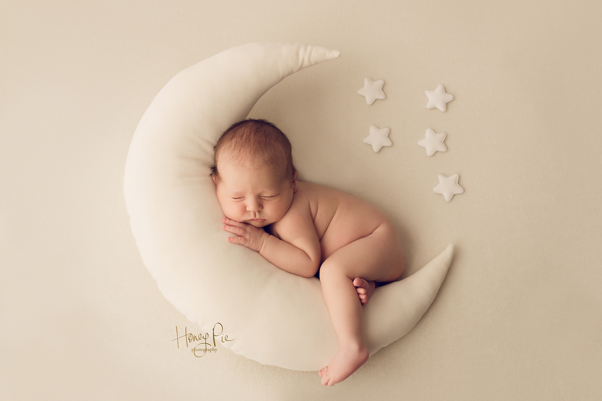 Newborn baby boy sleeping on a cream moon pillow surrounded by stars during his baby photoshoot in brighton