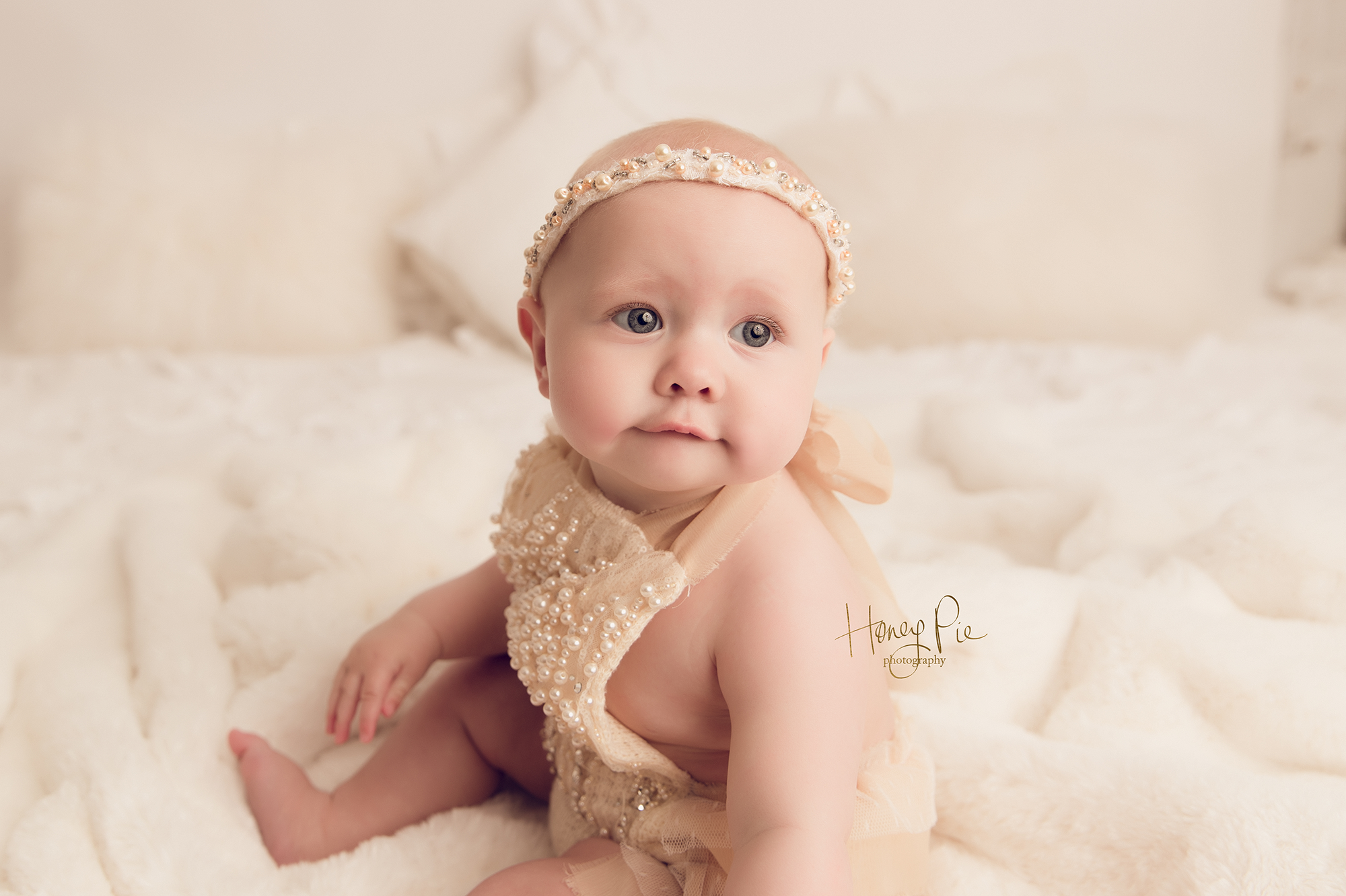 Baby girl wearing a pearl romper suit gazing off camera during her baby photoshoot