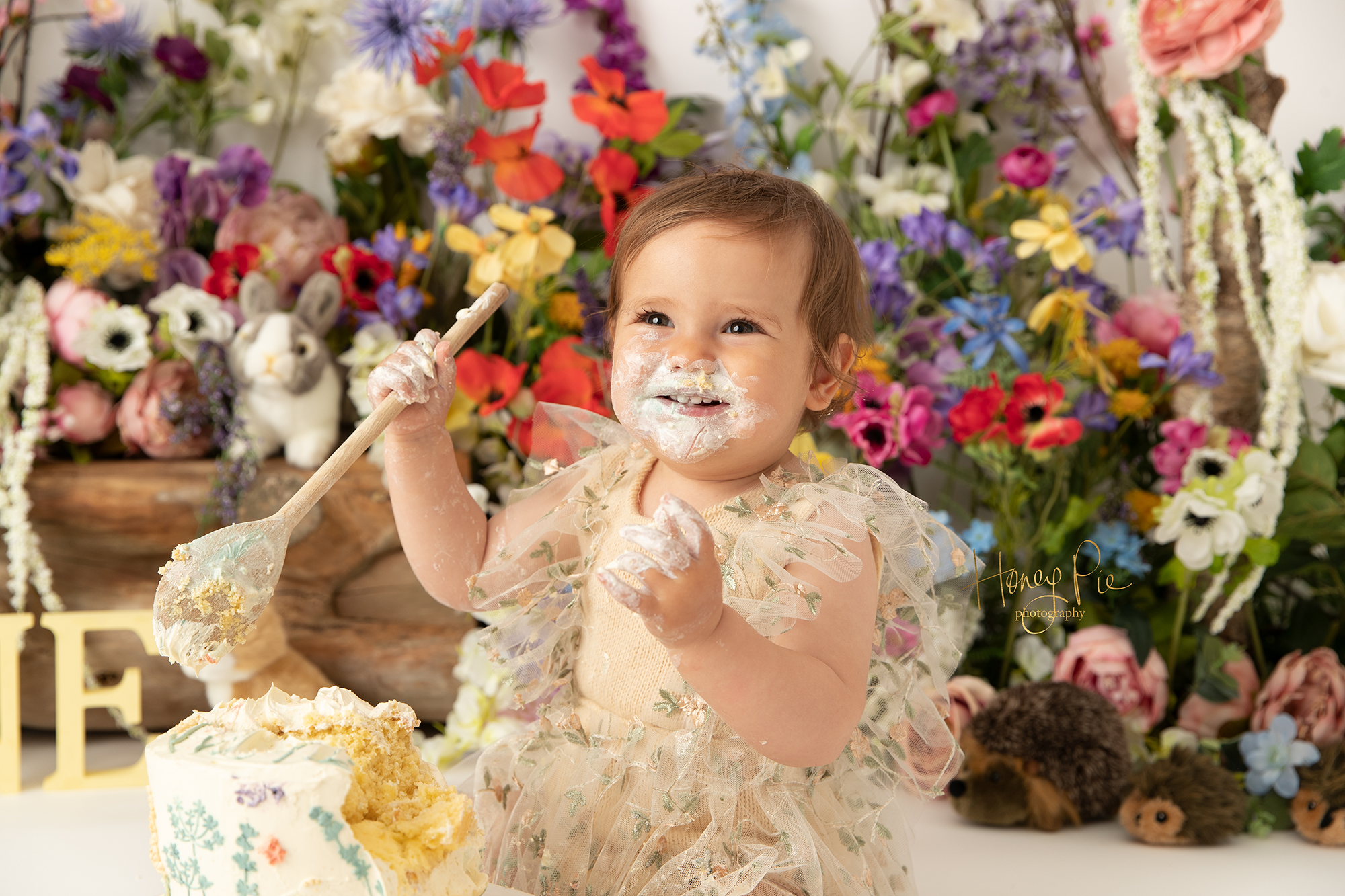 A smiling baby girl with cake all around her mouth & face during her 1st birthday cake smash photoshoot in sussex